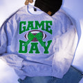 A heather gray crewneck sweatshirt with a 'GAME DAY' football graphic in green and brown, styled flat-lay with a black knit beanie and blue jeans on a white background.