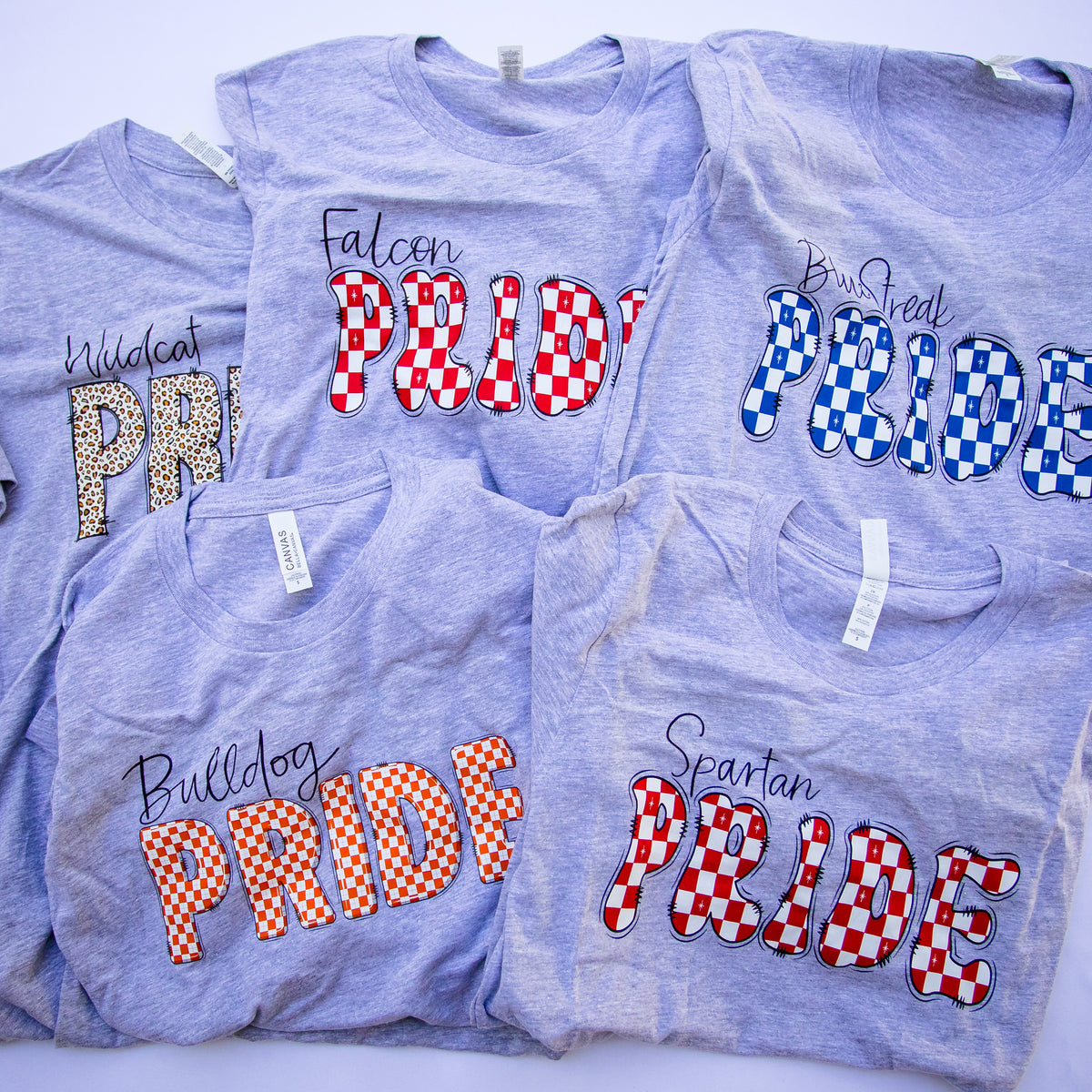 Five heather gray t-shirts with different collegiate-style 'Pride' graphics in red, white, blue, orange, and leopard print, arranged in a flat-lay collage.