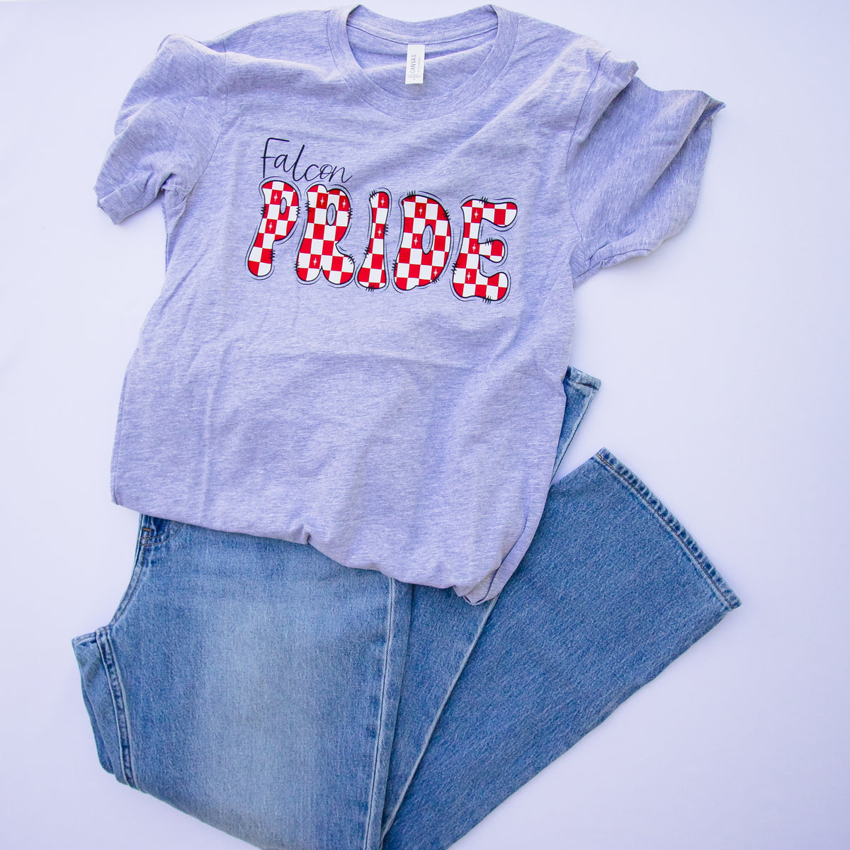 A light heather purple t-shirt with 'Falcon PRIDE' printed on the front, styled with folded blue jeans on a white background.