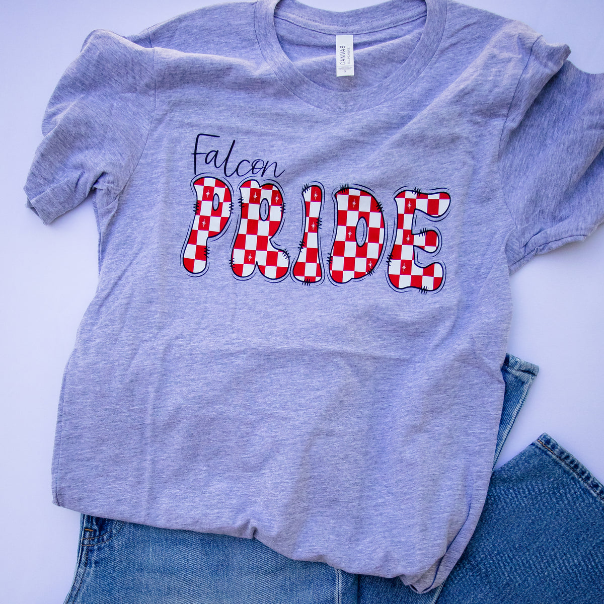 A heather gray t-shirt with 'Falcon PRIDE' printed on the front, styled flat-lay with blue jeans on a white background.