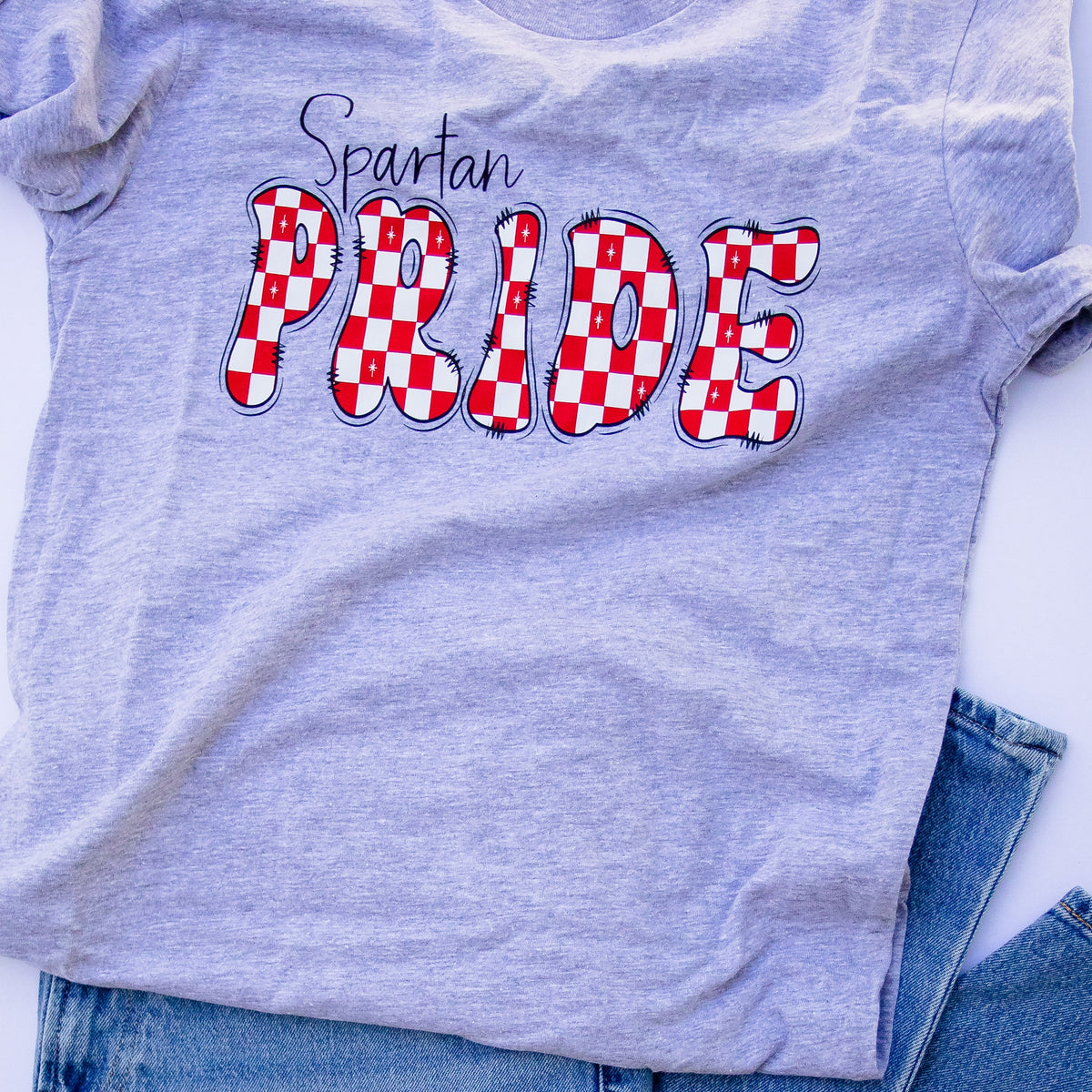 A light heather gray t-shirt with 'Spartan PRIDE' printed on the front, styled flat-lay on top of blue jeans against a white background.