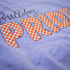 Close-up of a light lavender-purple t-shirt featuring a large orange and white checkered 'PRIDE' graphic with a black script 'Bulldog' above it.