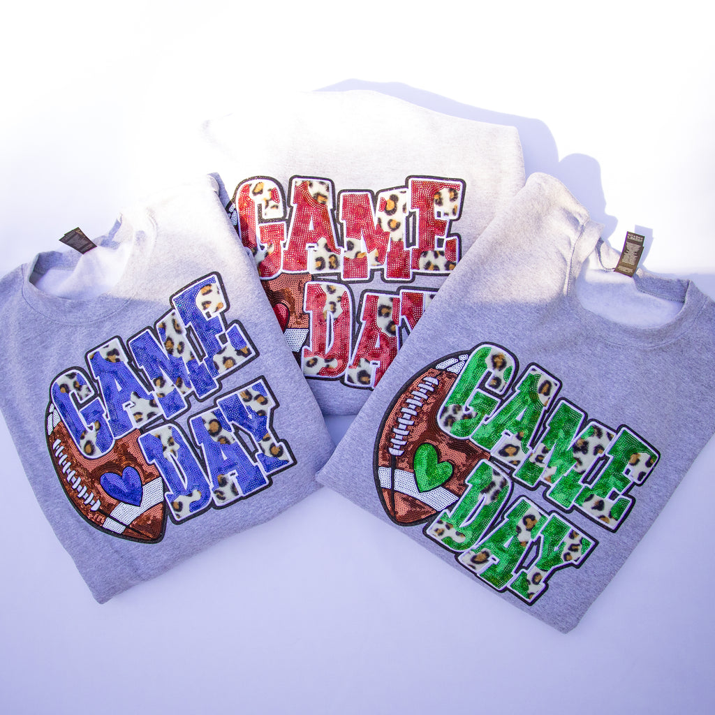 Three gray hoodies with 'GAME DAY' graphics in different colors (blue, red, green) and a football motif, arranged on a white background.