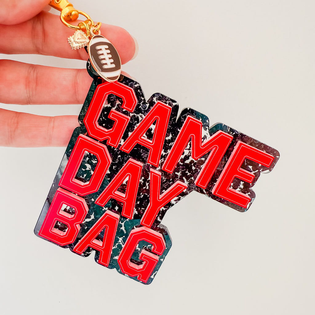 Keychain with 'Game Day Bag' text and football charm held by a hand on a light gray background by October House Co. in Hartville, Ohio.