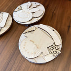 Unpainted laser-cut wooden ornaments or craft pieces arranged on a wooden tabletop, including a snowman face, star, oval shapes, and a snowflake detail.