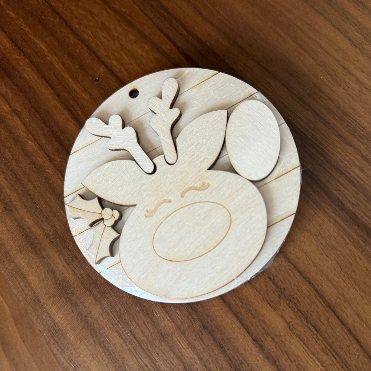 A round wooden ornament or decorative piece with laser-cut reindeer features, including antlers, a nose, and hooves, displayed on a wooden tabletop.