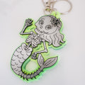 A mermaid-themed keychain featuring a Day of the Dead sugar skull mermaid with a green translucent outline and silver metal keyring.