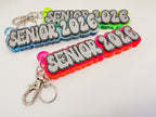 Three acrylic keychains with 'SENIOR 2026' text in different neon color combinations, shown on a plain white background.