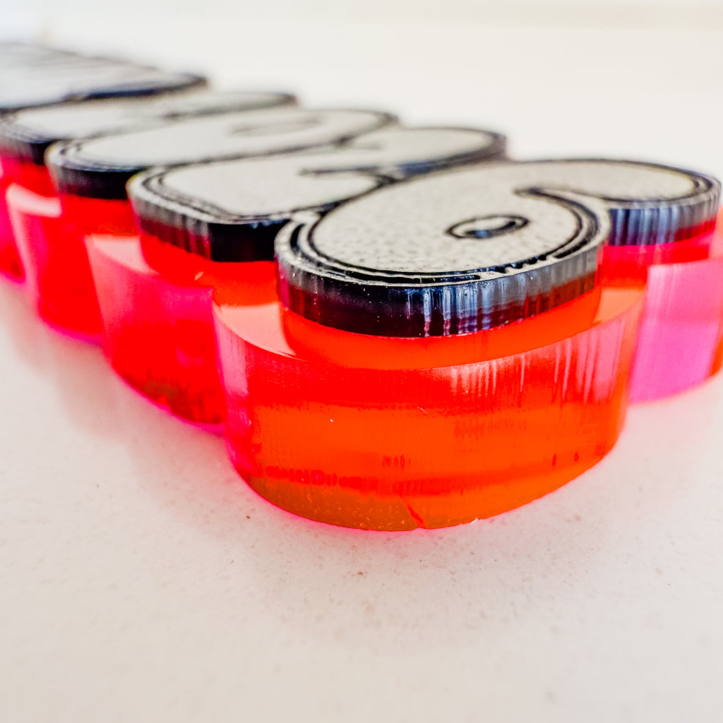 A close-up of a translucent acrylic letter sign spelling '2026' in bright red and orange, with black backing and clear acrylic tops, resting on a light surface.