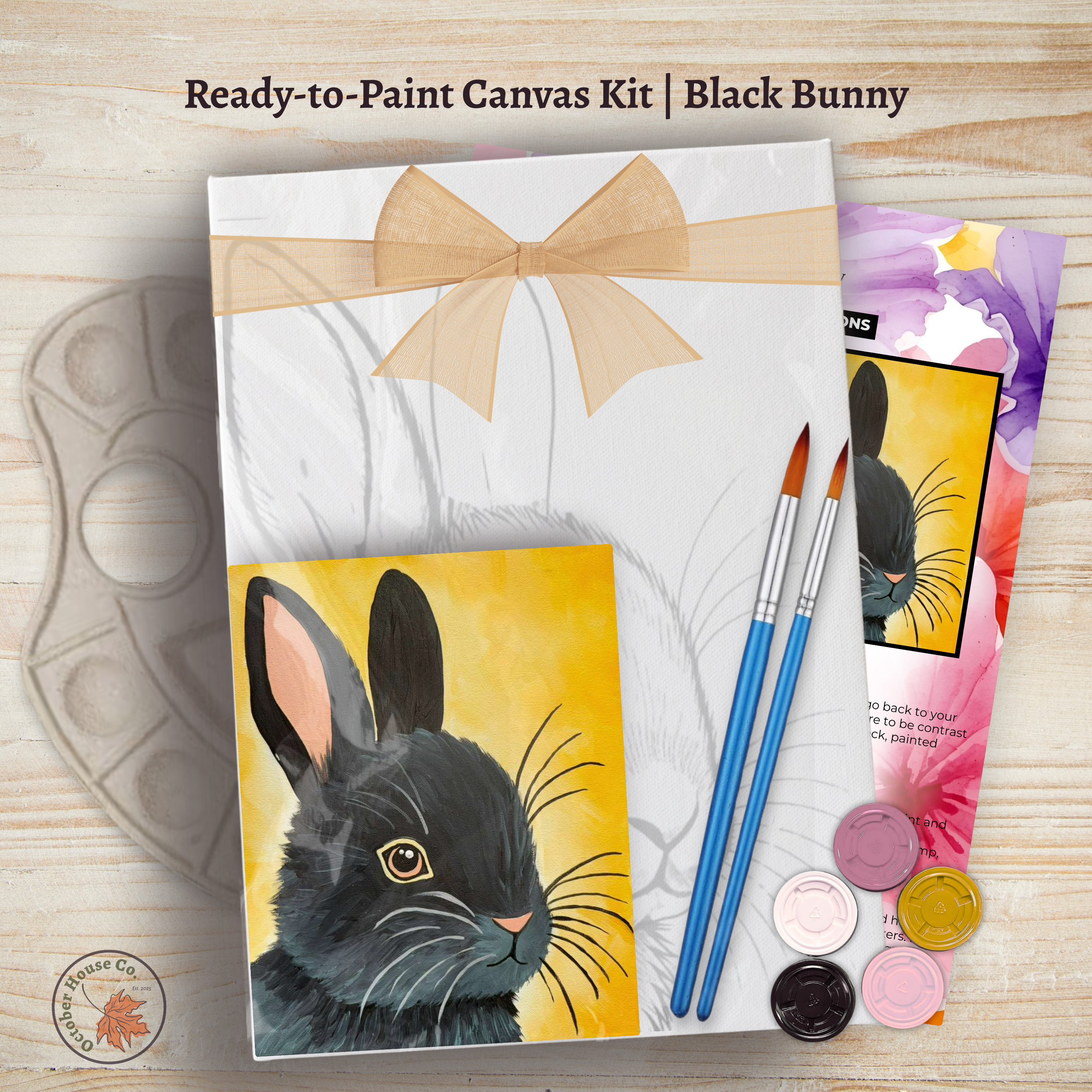 Ready-to-paint canvas kit with black bunny design, paintbrushes, and paint on a wooden surface by October House Co. in Hartville, Ohio.
