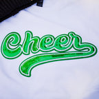 A close-up of a white t-shirt featuring a large, cursive 'Cheer' graphic embellished with green sequins and a white outline.