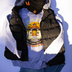 A styled flat-lay of a light blue graphic sweatshirt layered under a black puffer vest with light gray lining, accessorized with a black knit beanie and blue jeans against a white background.